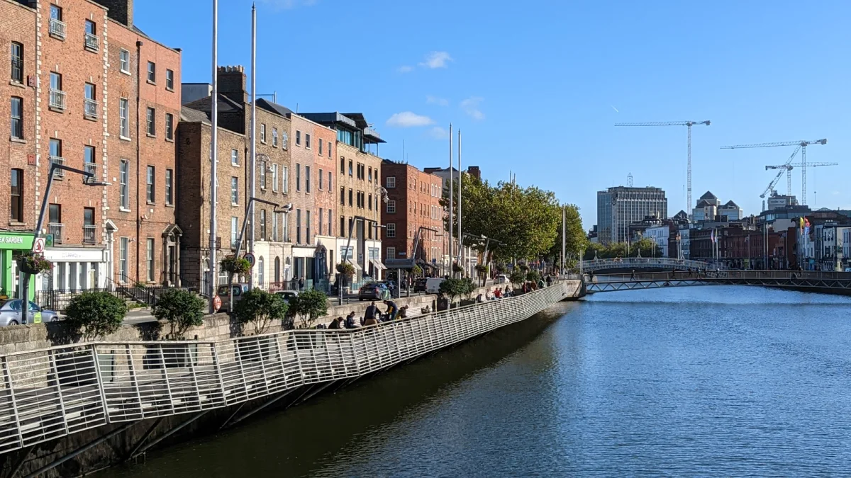 Sunny day on the River Liffey in Dublin, people sitting on the bank with the city behind.