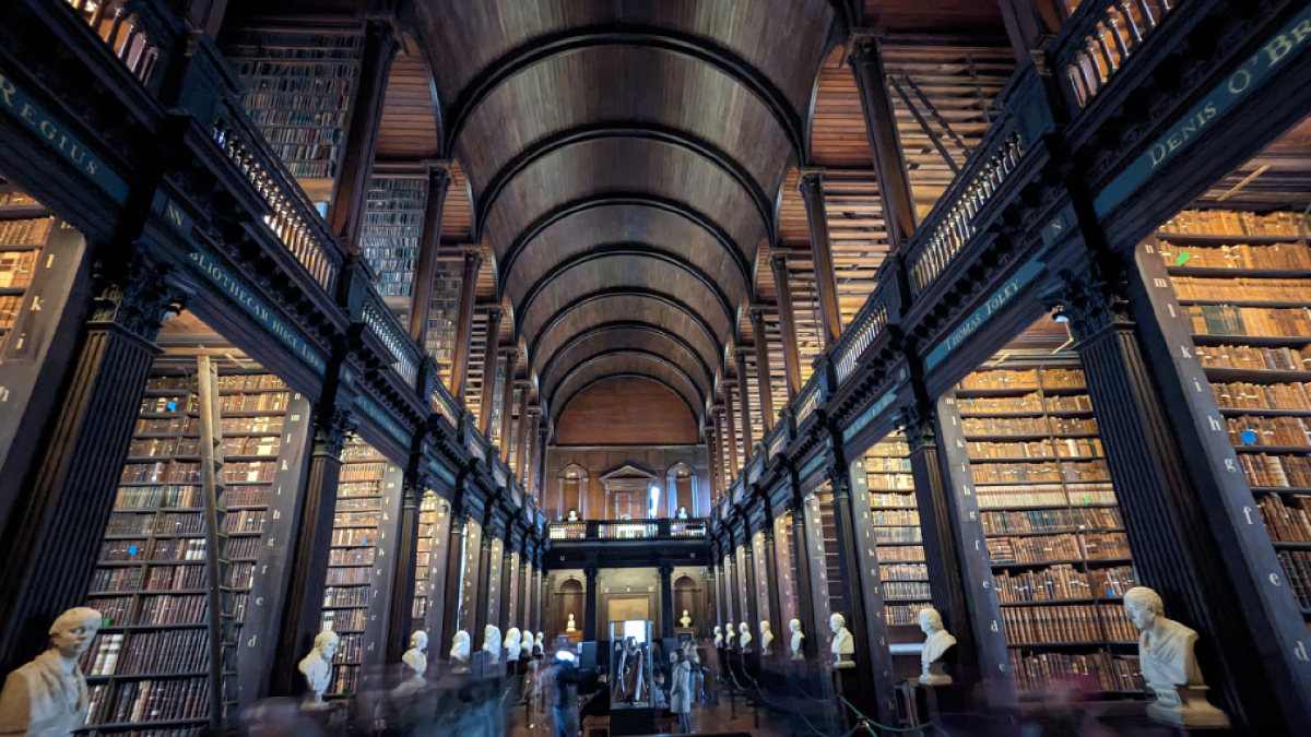 Η Long Room Library στο Trinity College στο Δουβλίνο, με ξύλινη καμάρα, προτομές φιλοσόφων και χιλιάδες παλιά βιβλία σε ψηλά ράφια.