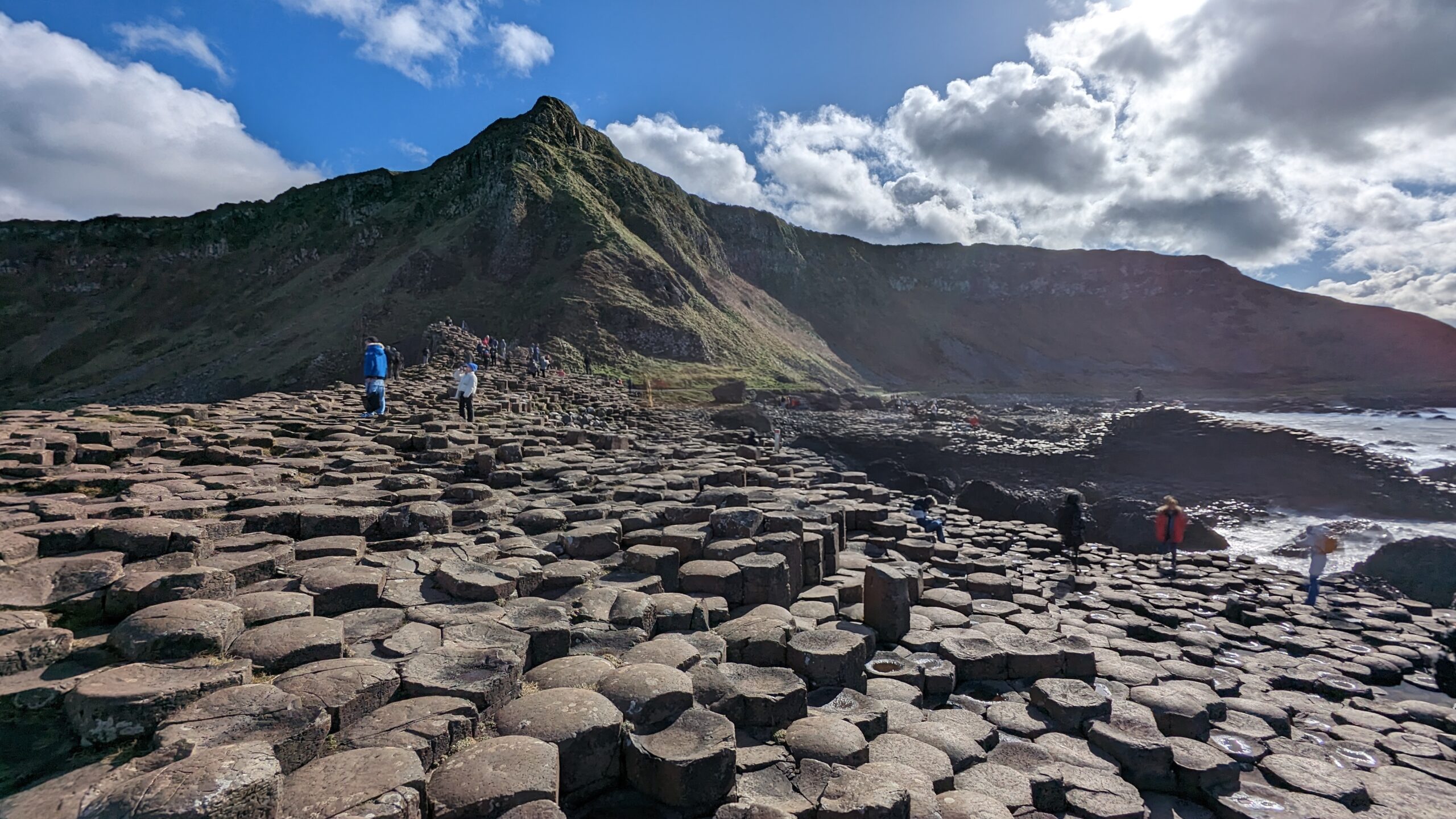 Bασάλτες στο Giant’s Causeway στη βόρεια Ιρλανδία με ταξιδιώτες να περπατούν δίπλα στη θάλασσα.