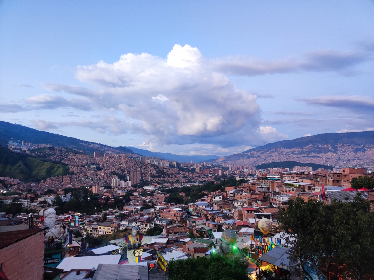 Πανοραμική άποψη της γειτονιάς Comuna 13 στο Μεδεγίν Κολομβίας, με πολύχρωμα σπίτια και τον ουρανό γεμάτο σύννεφα.