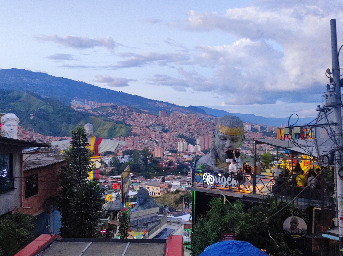 Η Comuna 13 στο Μεδεγίν με τα γλυπτά και την πόλη στο βάθος το σούρουπο.