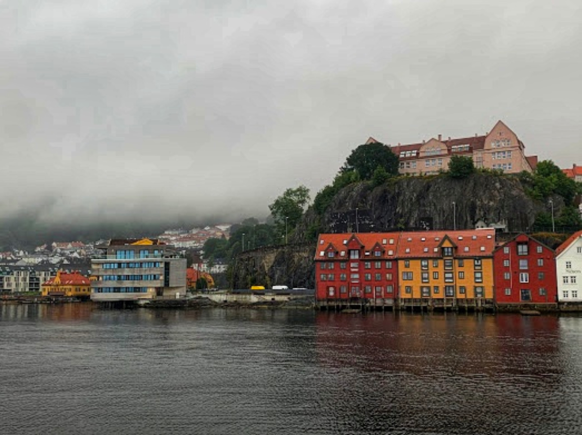Πολύχρωμα σπίτια δίπλα στο νερό στο Μπέργκεν με βουνό και ομίχλη στο φόντο μια βροχερή μέρα