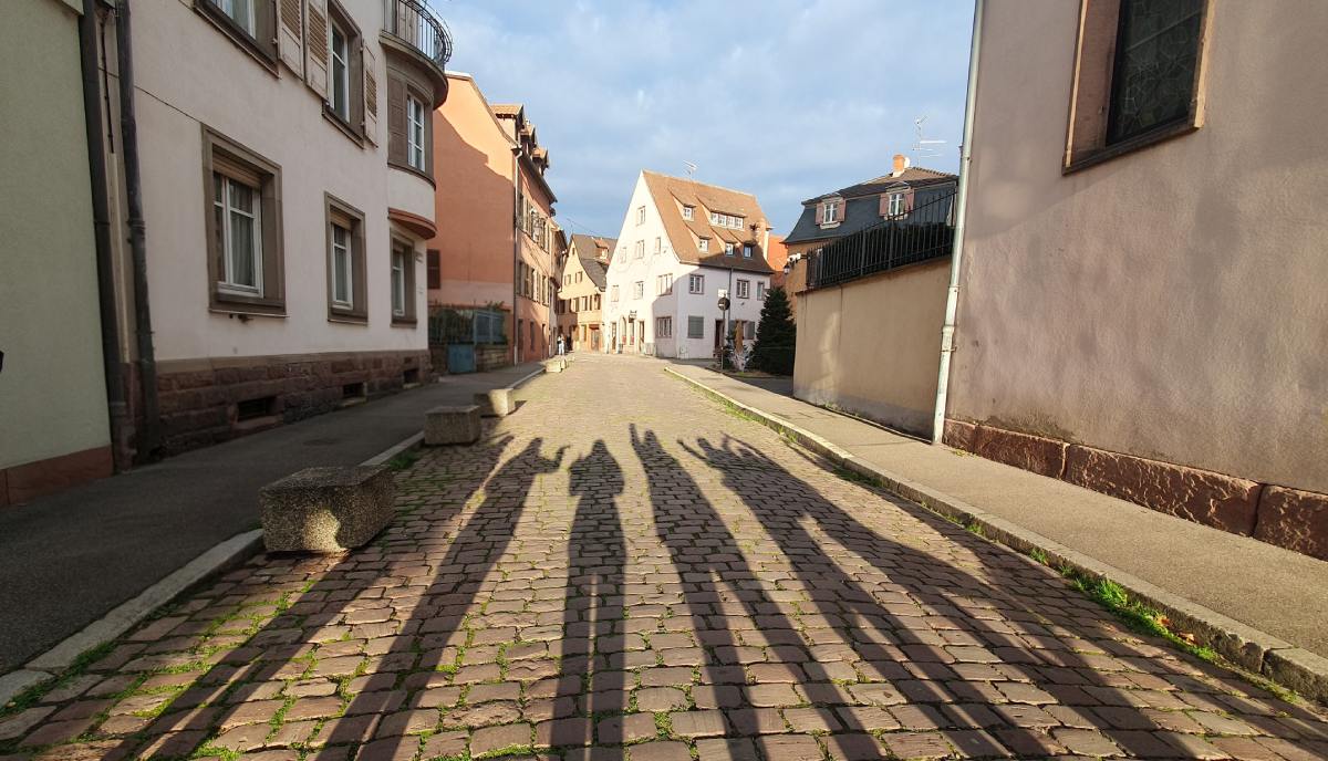 Πρωινό φως και σκιές παρέας σε πέτρινο δρόμο.
