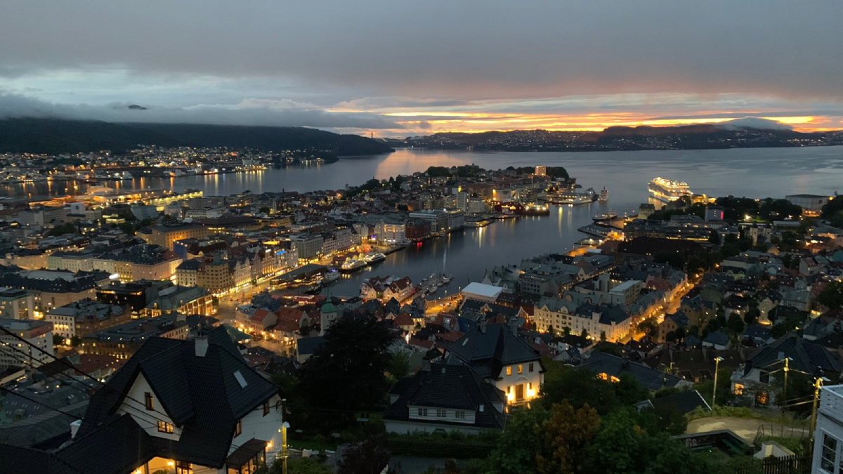 Νυχτερινή πανοραμική θέα στο Μπέργκεν με φωτισμένα κτίρια, λιμάνι και φιόρδ την ώρα του ηλιοβασιλέματος