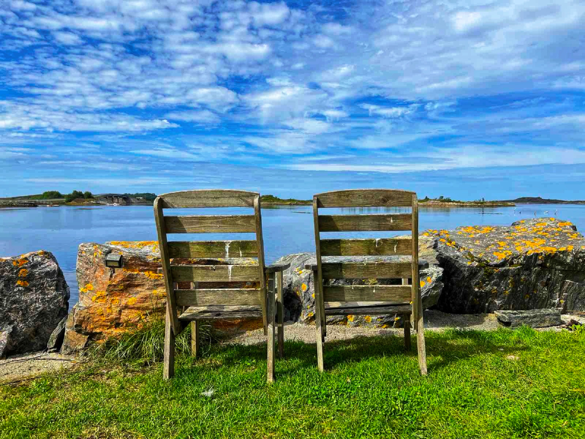 Δύο καρέκλες μπροστά στη θάλασσα, σε μια ήσυχη ταξιδιωτική εικόνα που αποτυπώνει την παρέα, τη στάση και εκείνες τις στιγμές που δεν θέλεις να τελειώσουν.