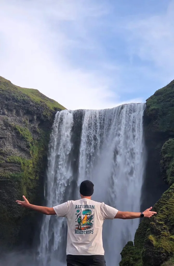 Ταξιδιώτης με ανοιχτά χέρια μπροστά στον Skogafoss
