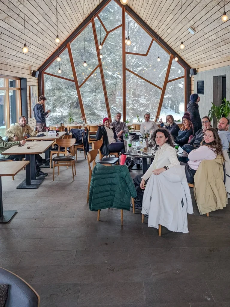 Η παρέα στο τραπέζι, σε ξύλινο lodge με τζαμαρία στο χιόνι